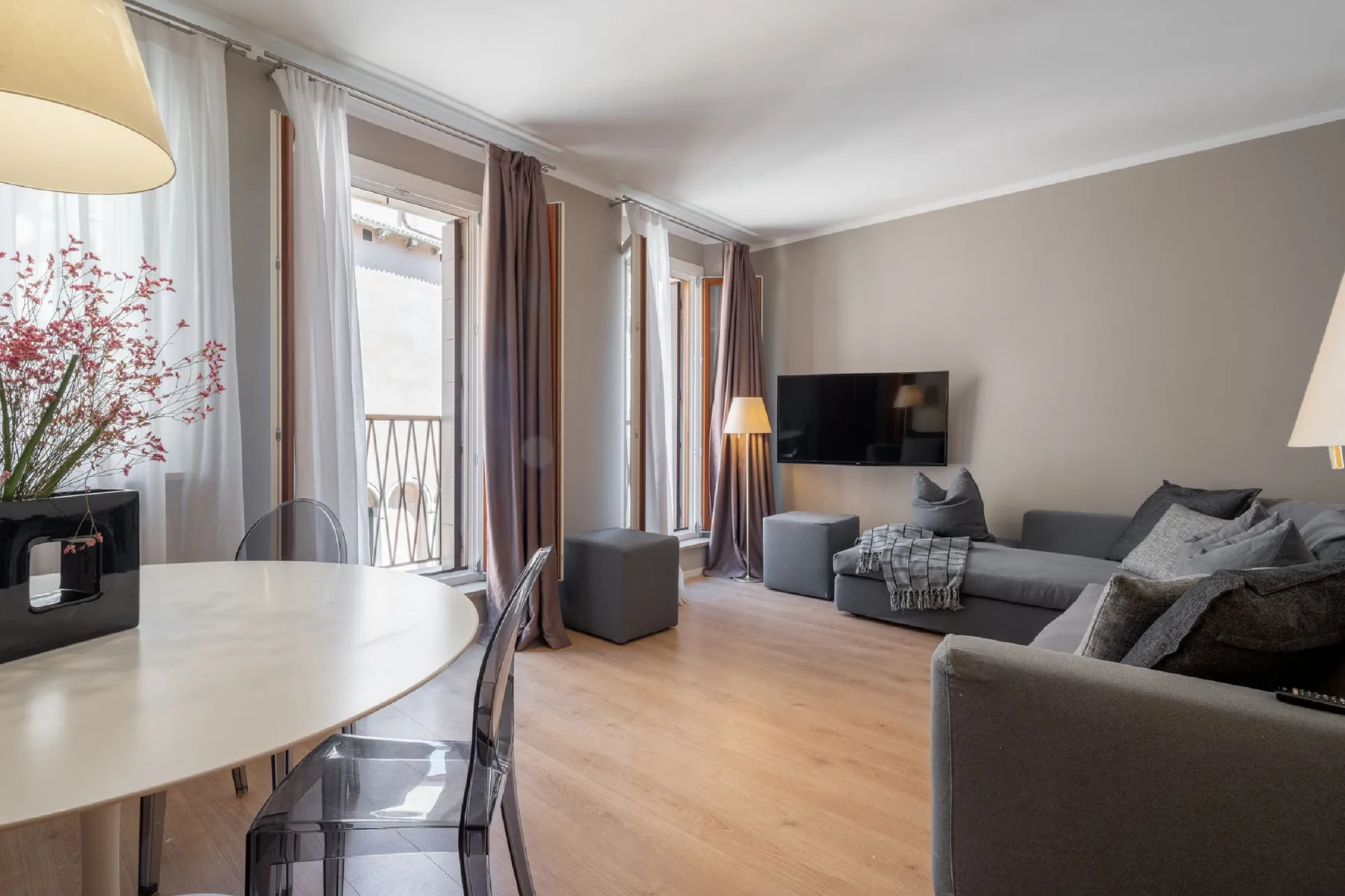 Una sala de estar con mesa de comedor, asientos y ventanas altas.