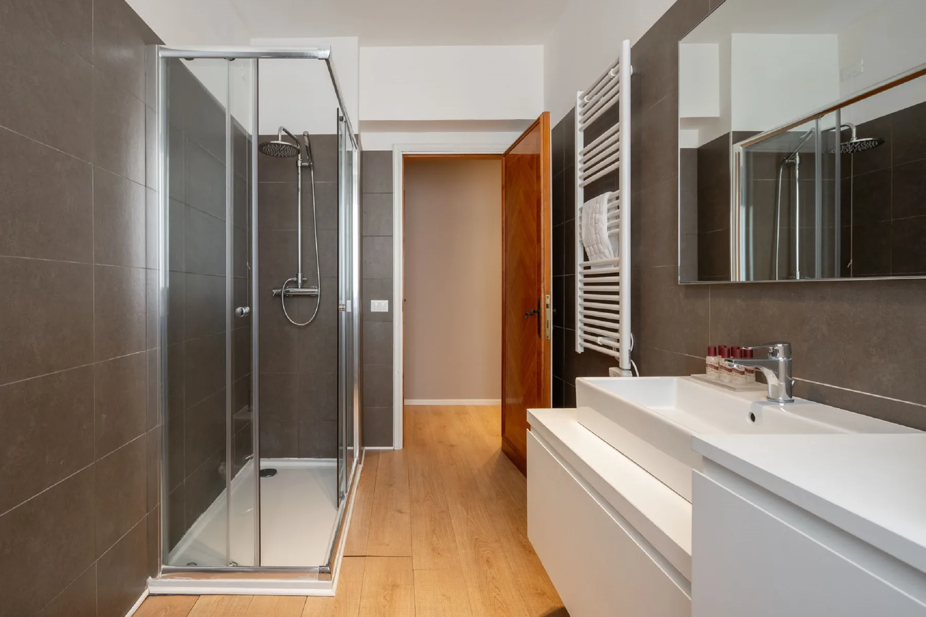 A bathroom with a glass shower, sink, and wooden flooring.