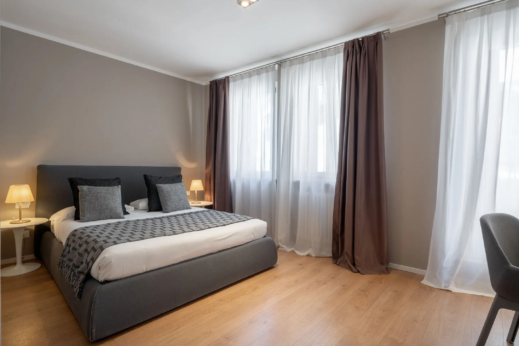 A bedroom with a bed, bedside lamps, and tall windows with curtains.