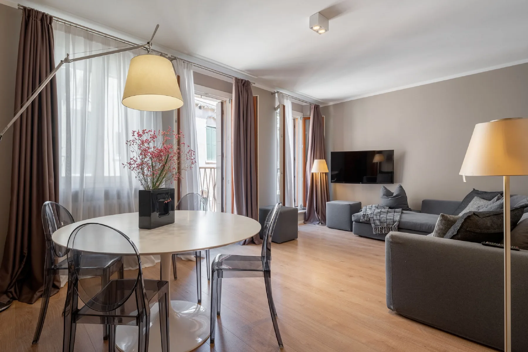 Una sala de estar con una mesa de comedor junto a ventanas altas y asientos.