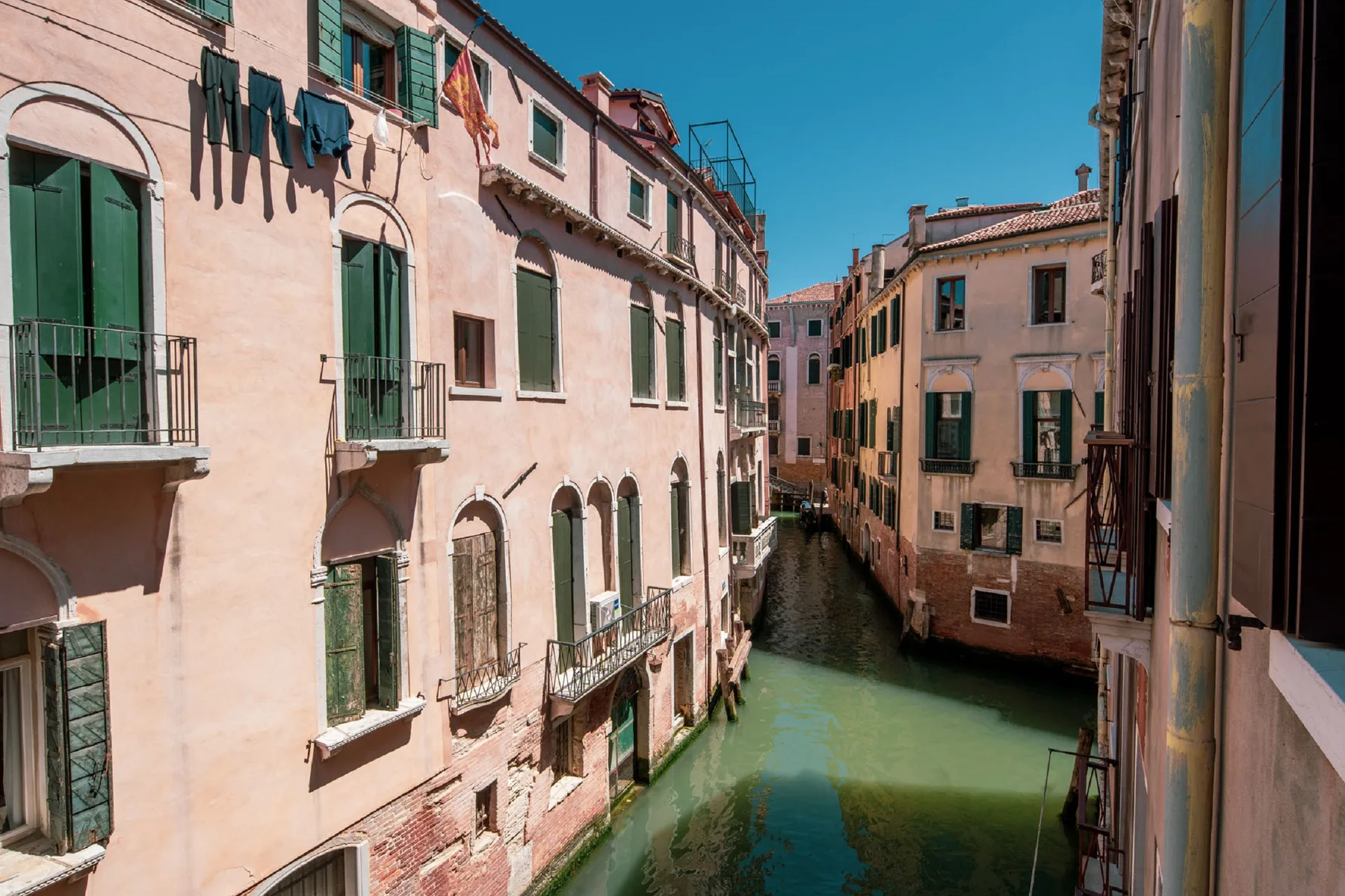 A narrow canal runs between closely spaced buildings in a sunlit urban scene.