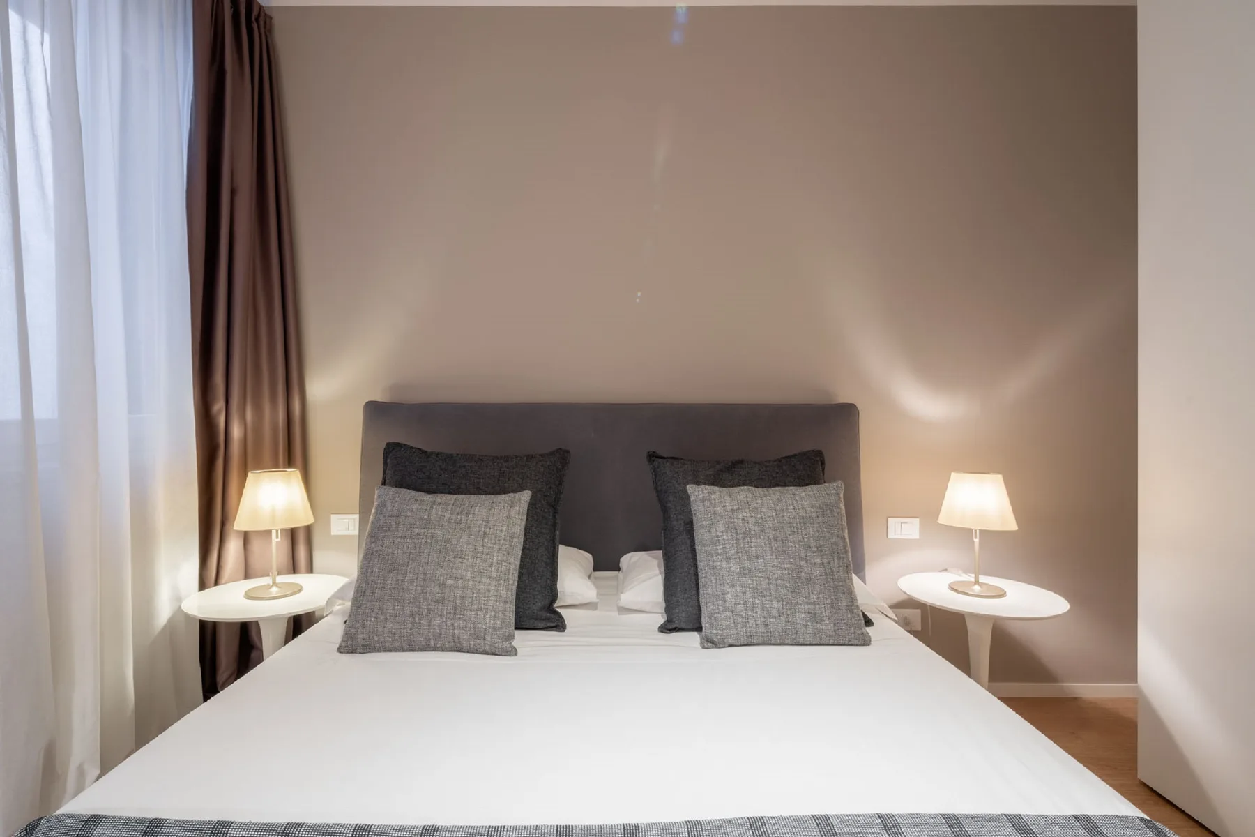 A bedroom with a neatly made bed, gray pillows, and matching bedside lamps.