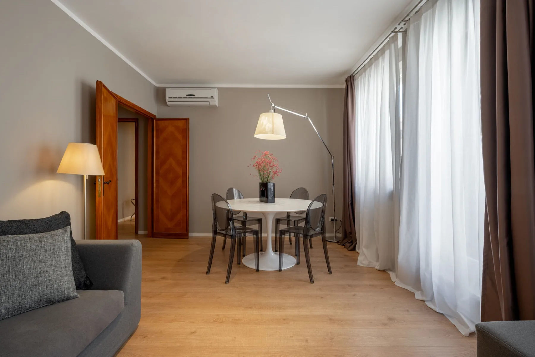 A dining area with a round table and tall curtained windows.