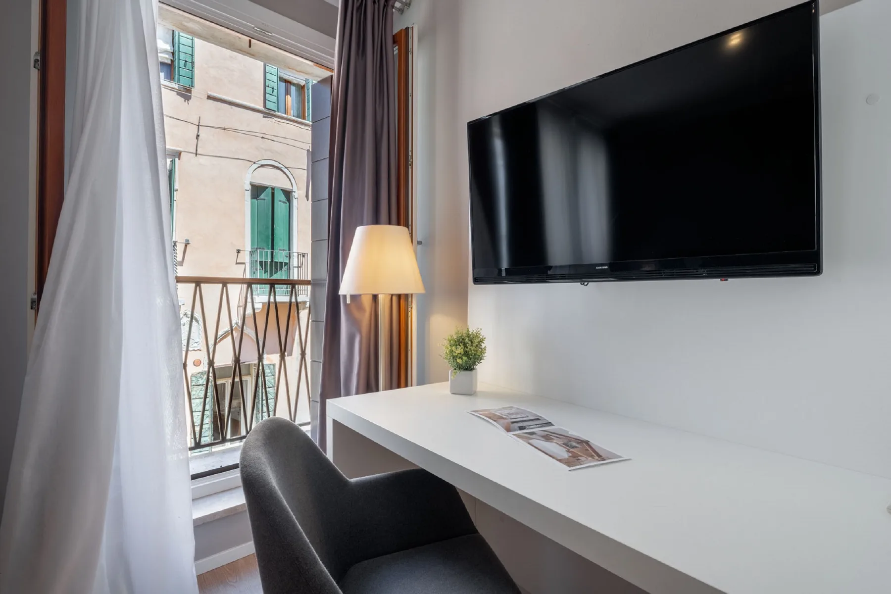 A desk and seating area with a wall-mounted television beside a curtained window.