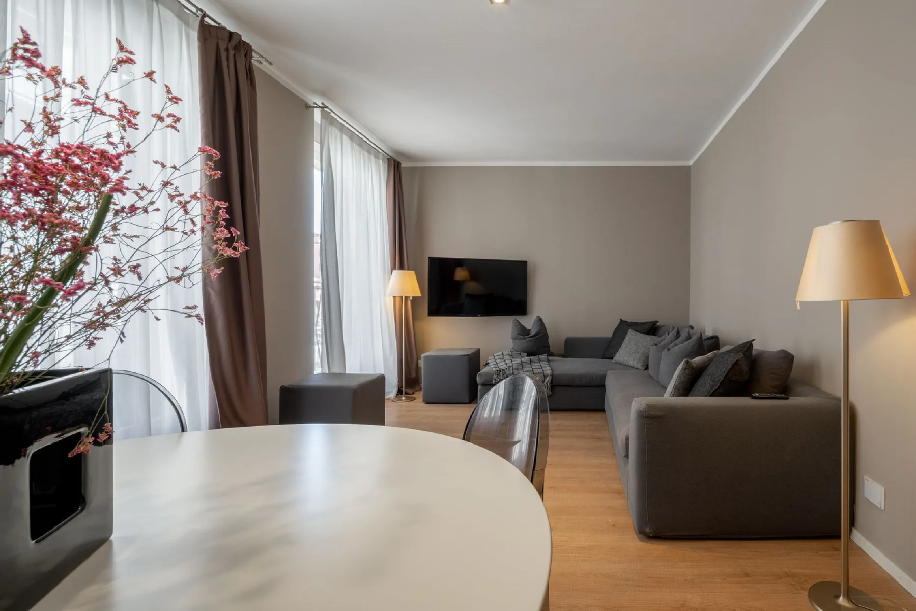 A living room with a gray sectional, wall-mounted television, and round dining table.