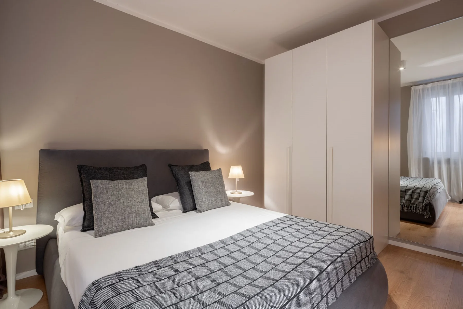 A bedroom with a neatly made bed and a floor-to-ceiling wardrobe.