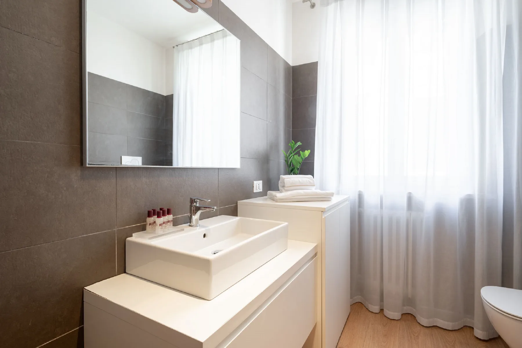 A bright bathroom with a sink, mirror, and sheer curtains.