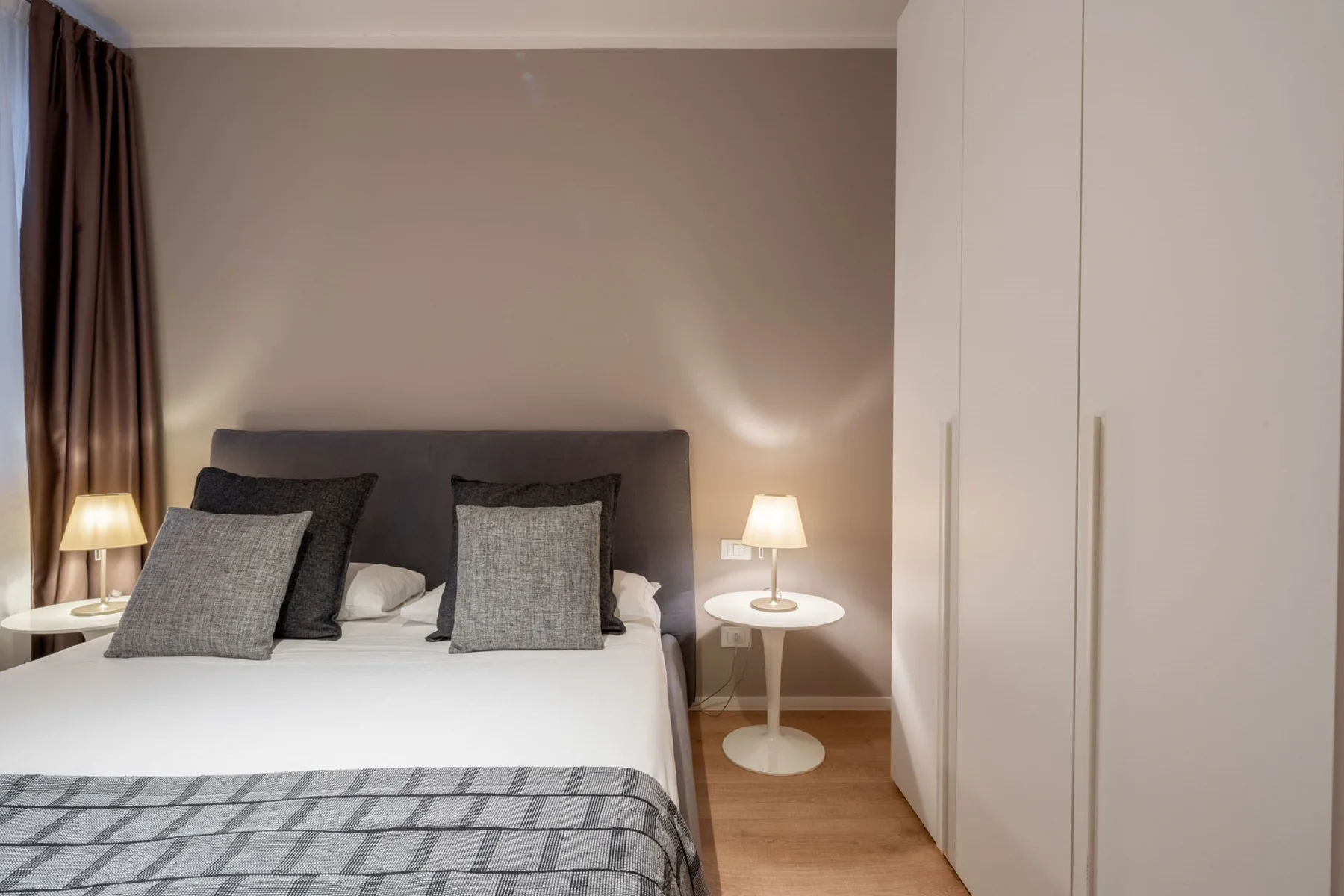A bedroom with a neatly made bed, bedside tables, and a wardrobe.