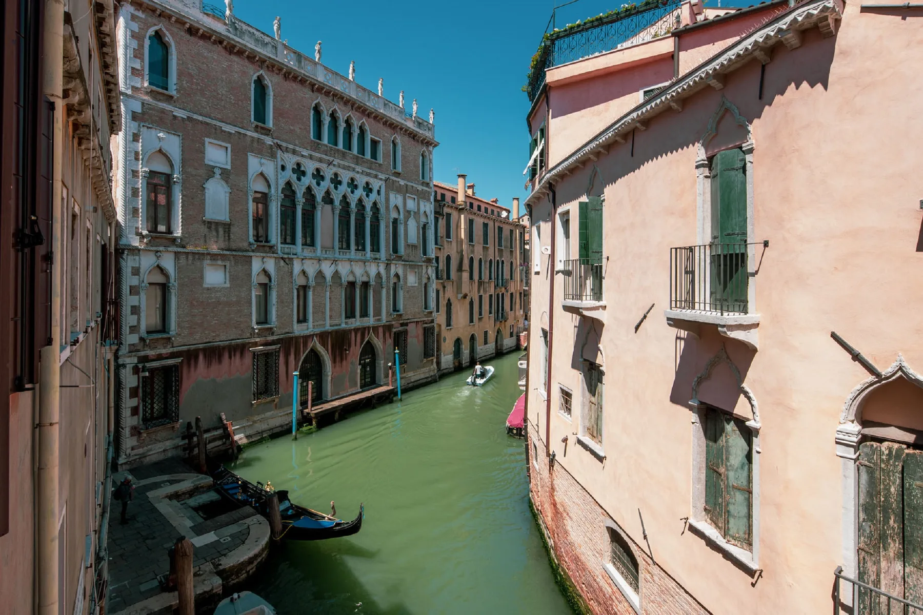 A narrow canal runs between historic buildings under a clear blue sky.