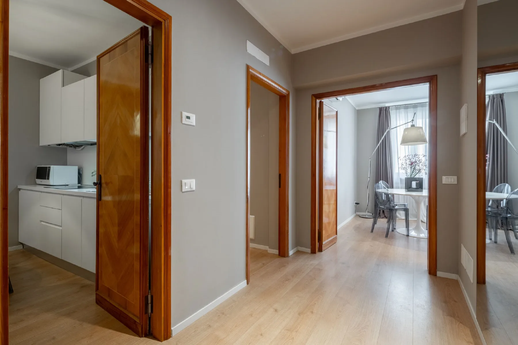 A hallway with wooden doorways opens onto a bright room with a table and chairs.