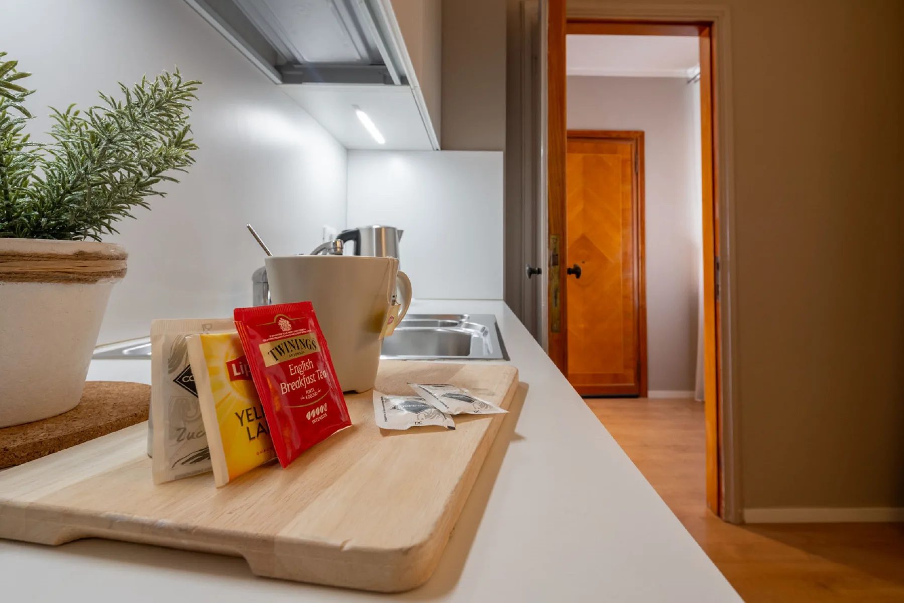 A kitchen counter with a potted plant and tea supplies beside the sink.
