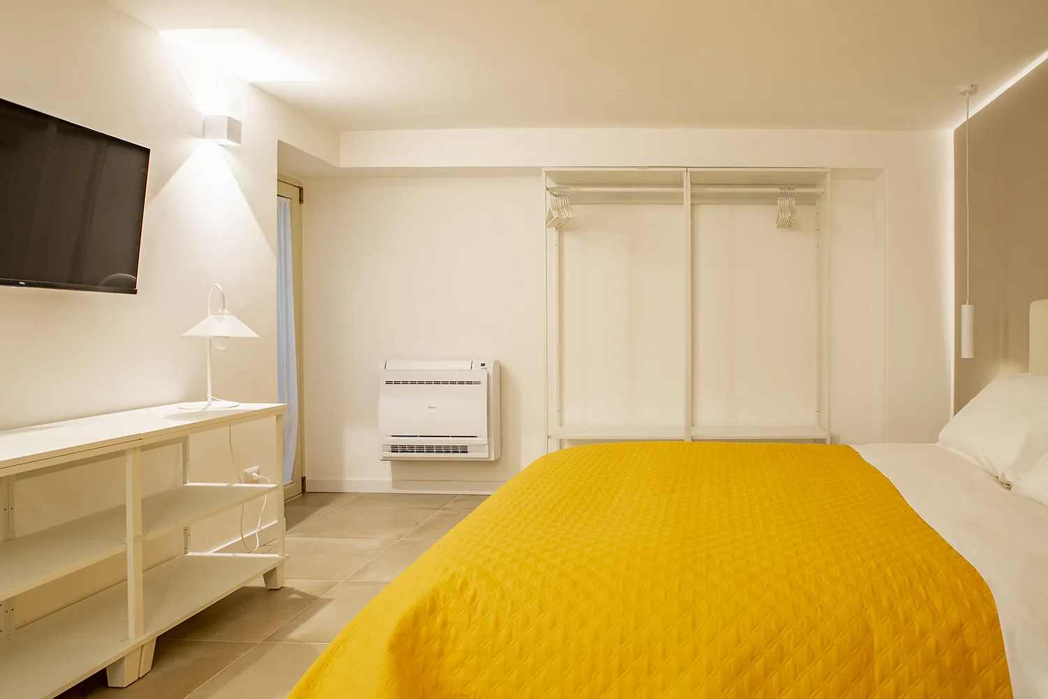 A bedroom with a bed covered by a bright yellow blanket and a wall-mounted television.