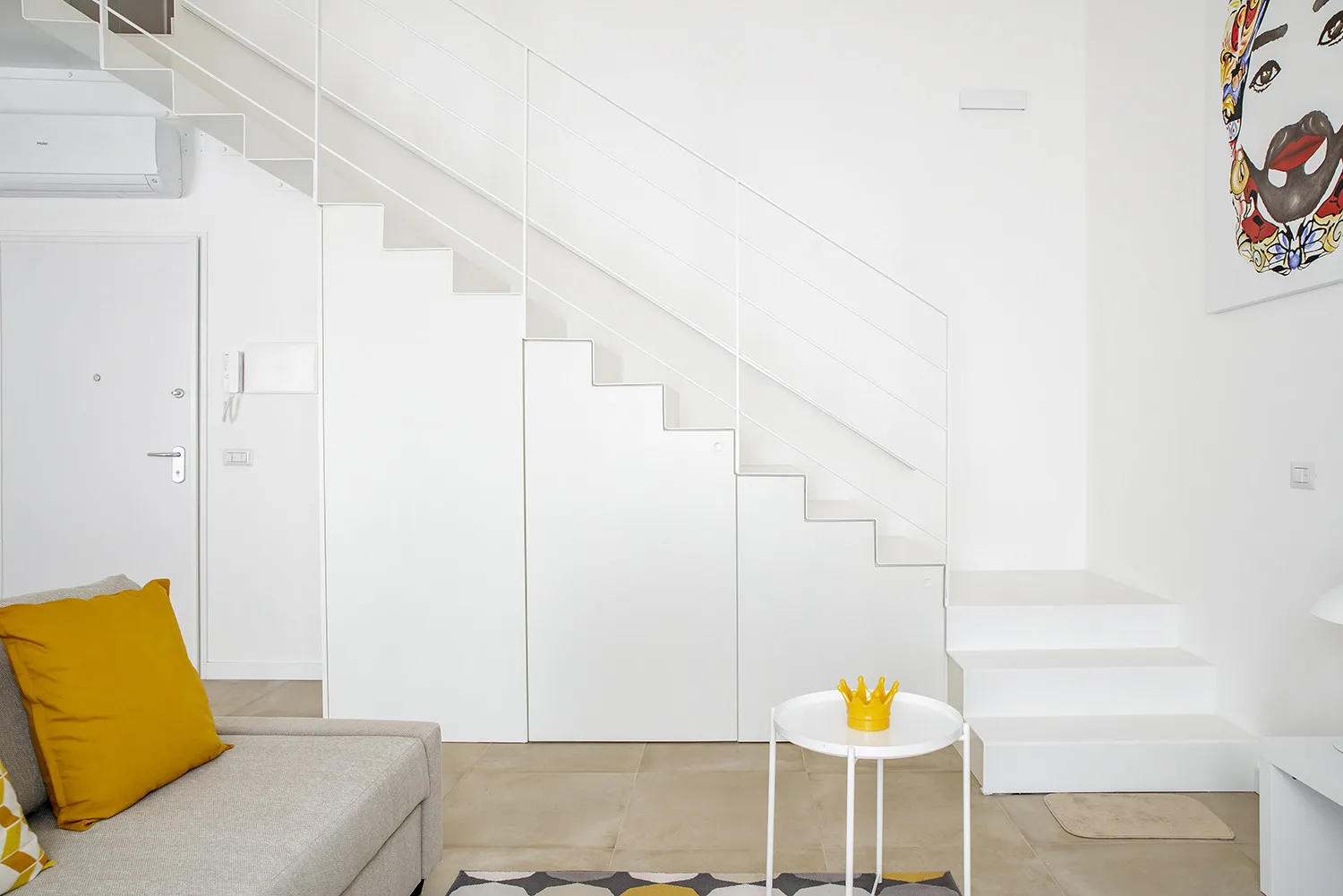A bright living area with a staircase, pale seating, and a small round table.
