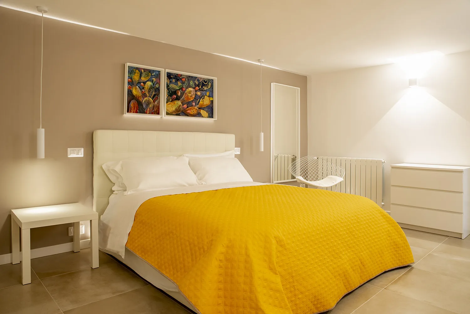 A bedroom with a bed covered by a bright yellow bedspread and colorful artwork above it.