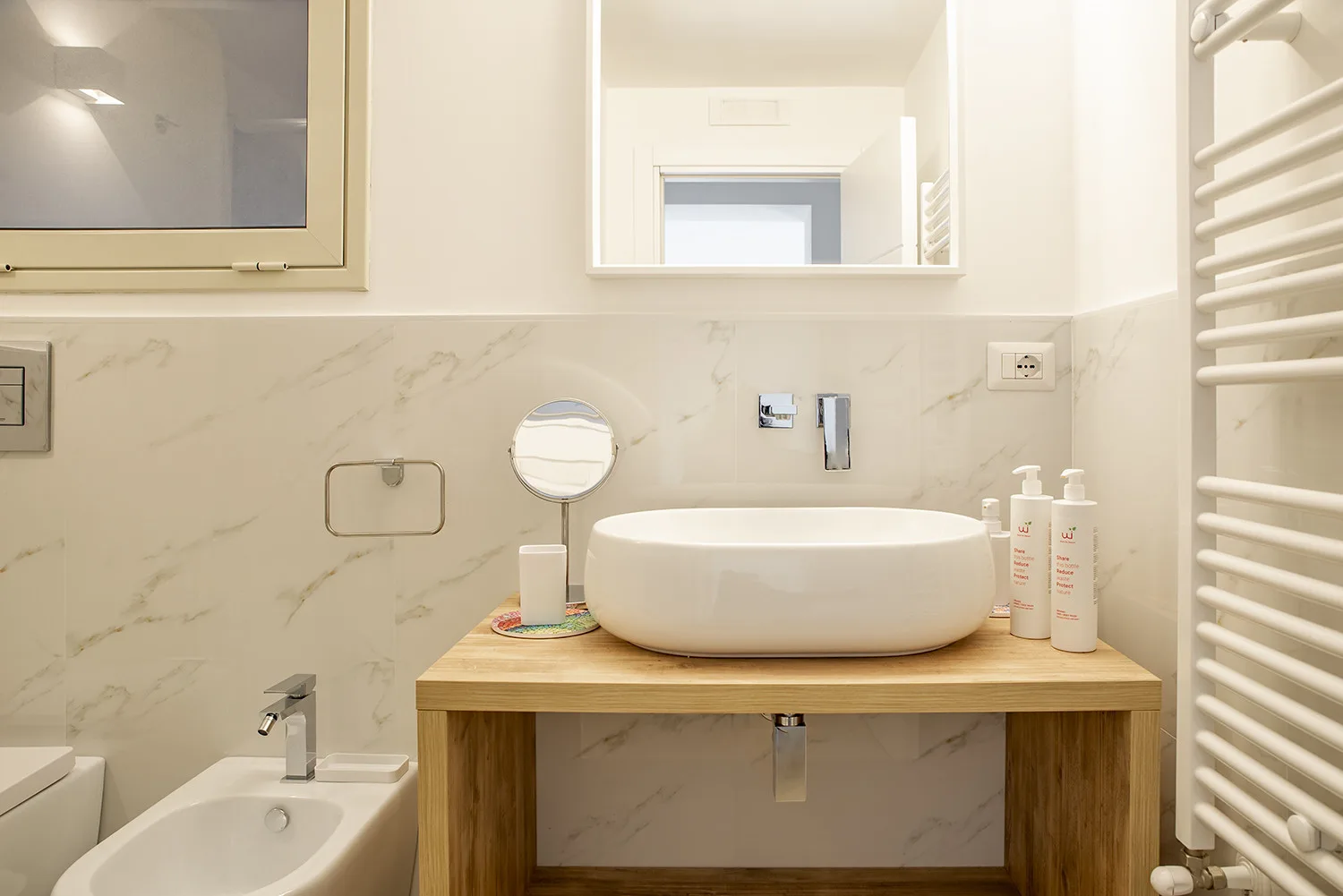 A bathroom vanity with a round basin, mirror, and white wall radiator.