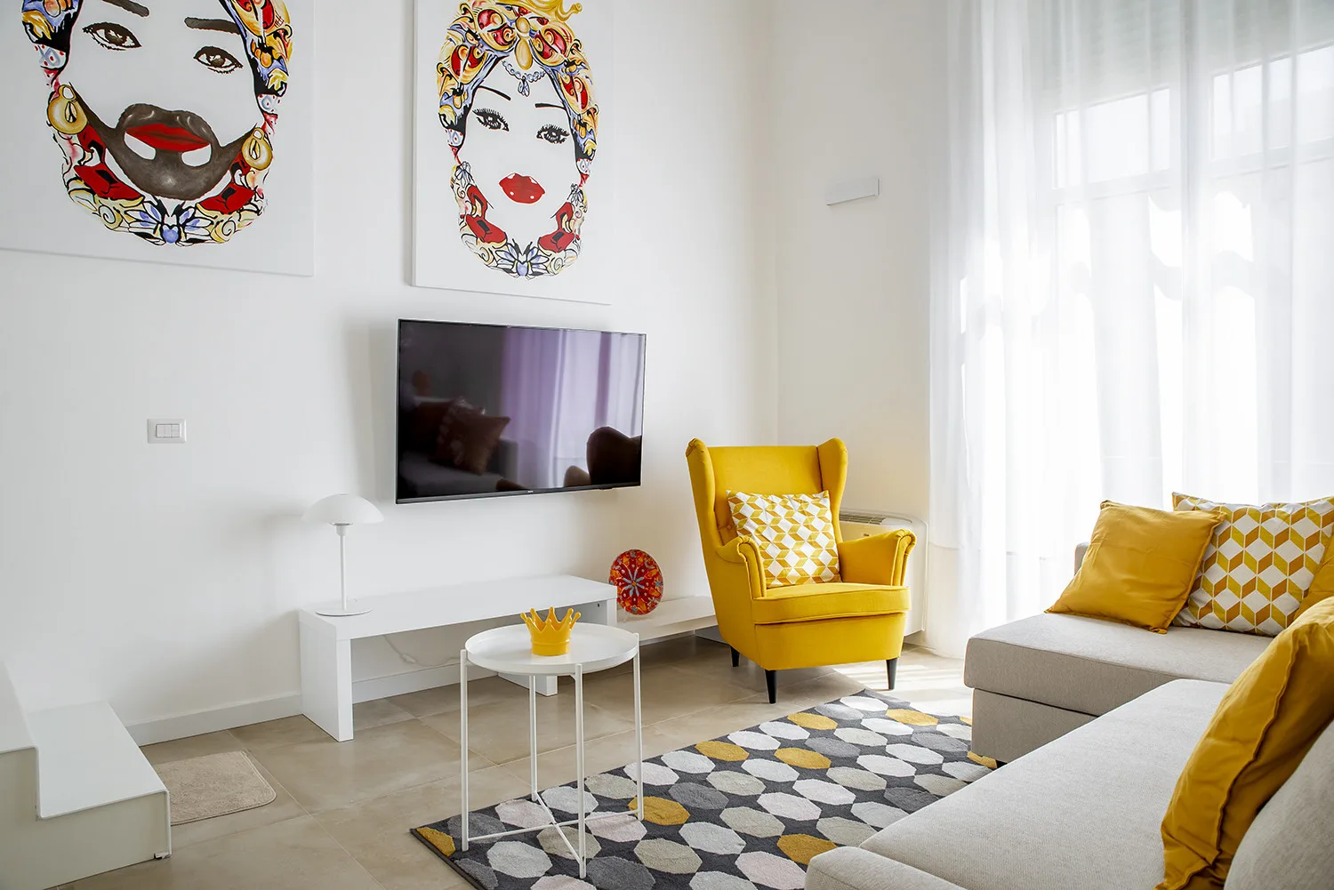 A bright living room with yellow seating and colorful artwork on the walls.