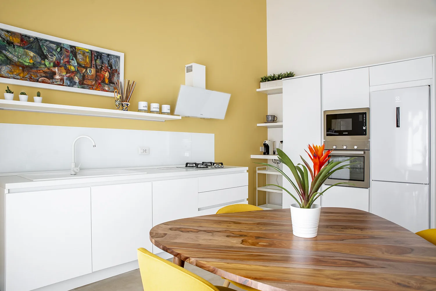 A bright kitchen with white cabinets, a cooktop, and a wooden dining table.