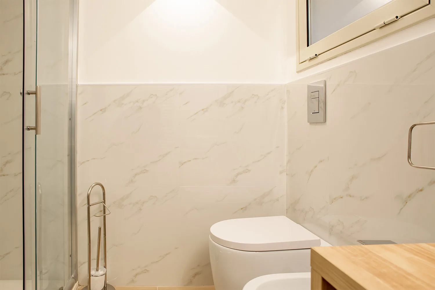 A bathroom with a toilet, a glass shower panel, and a wooden vanity.
