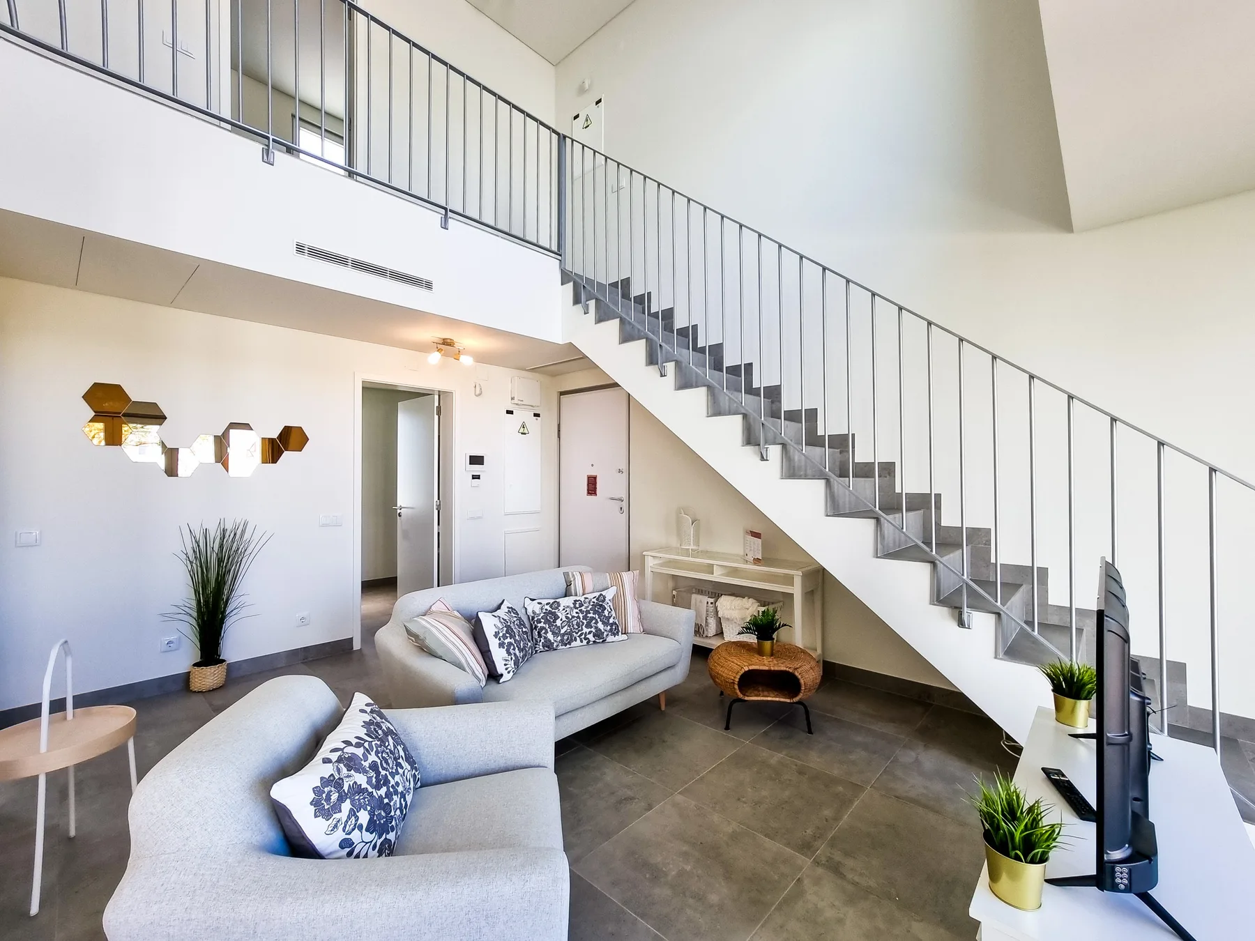 A bright living room with seating beneath a staircase and upper-level railing.