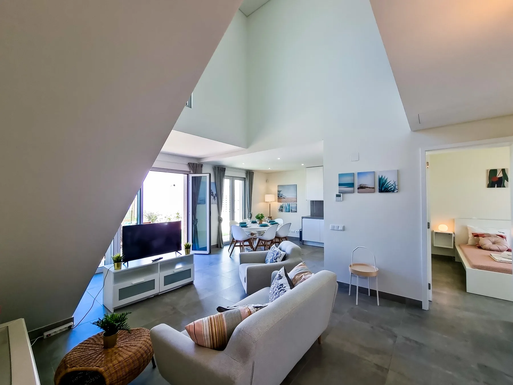 Una sala luminosa con asientos, un televisor y un comedor junto a grandes ventanas.