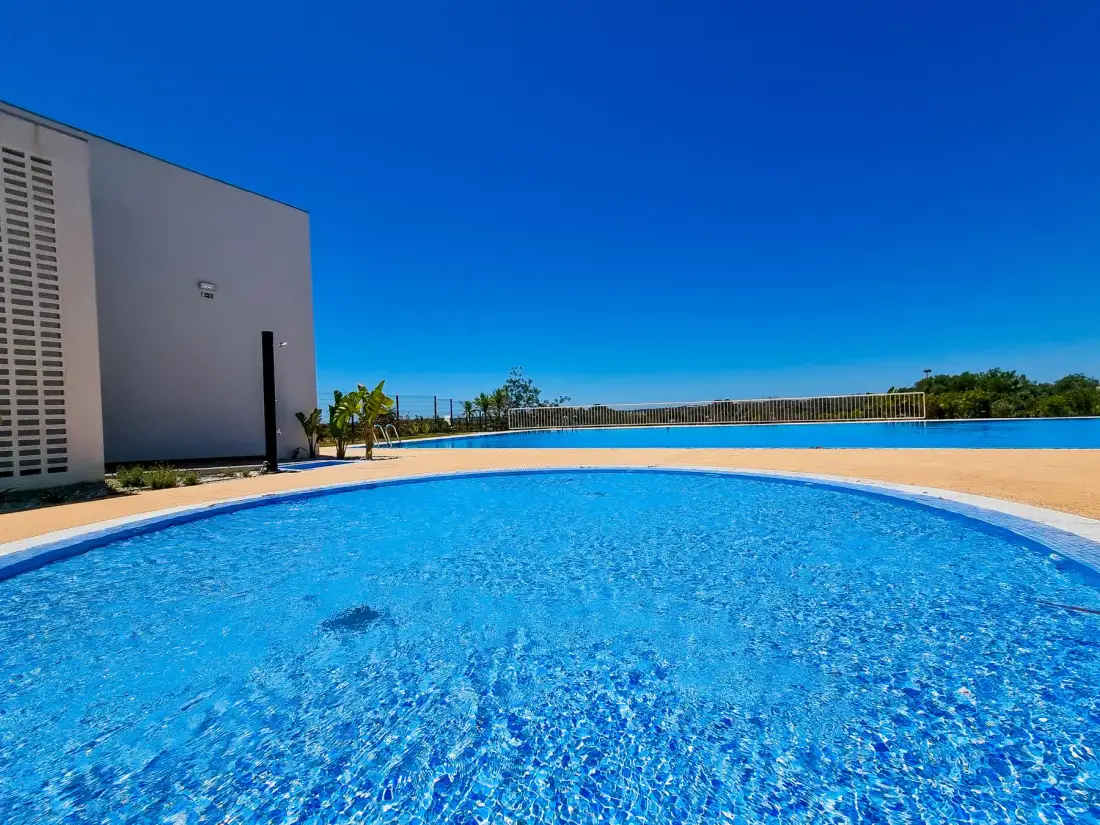Una piscina junto a un edificio moderno bajo un cielo azul despejado.