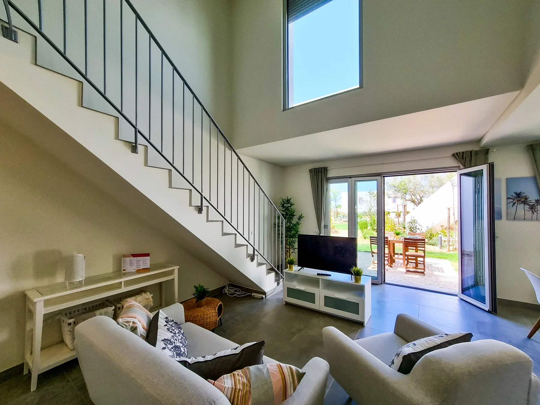 Una sala luminosa con una escalera y puertas abiertas a un patio.