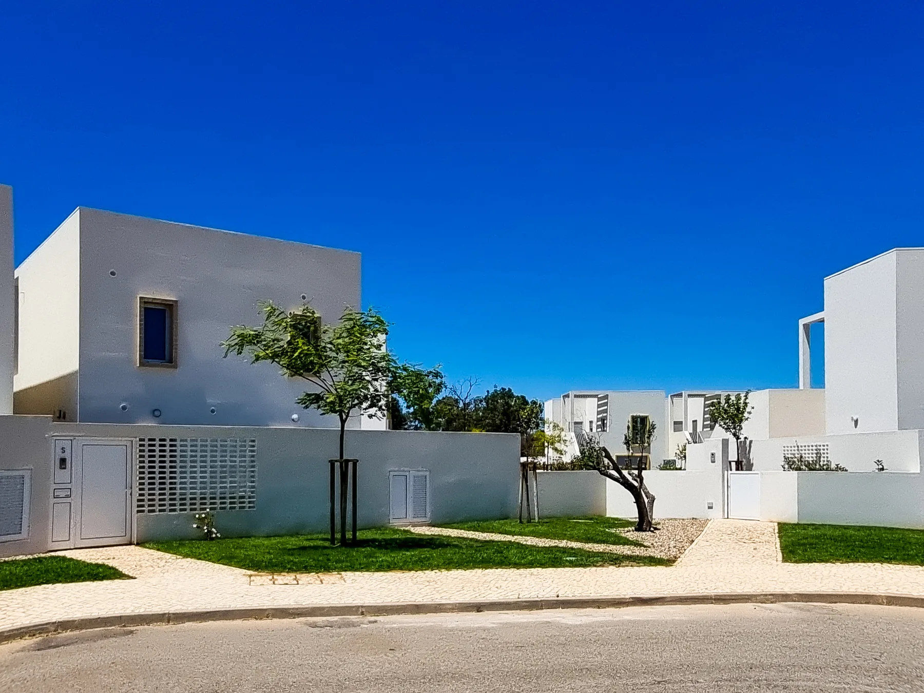 Una fila de edificios blancos modernos da a un sendero pavimentado y una pequeña zona ajardinada.