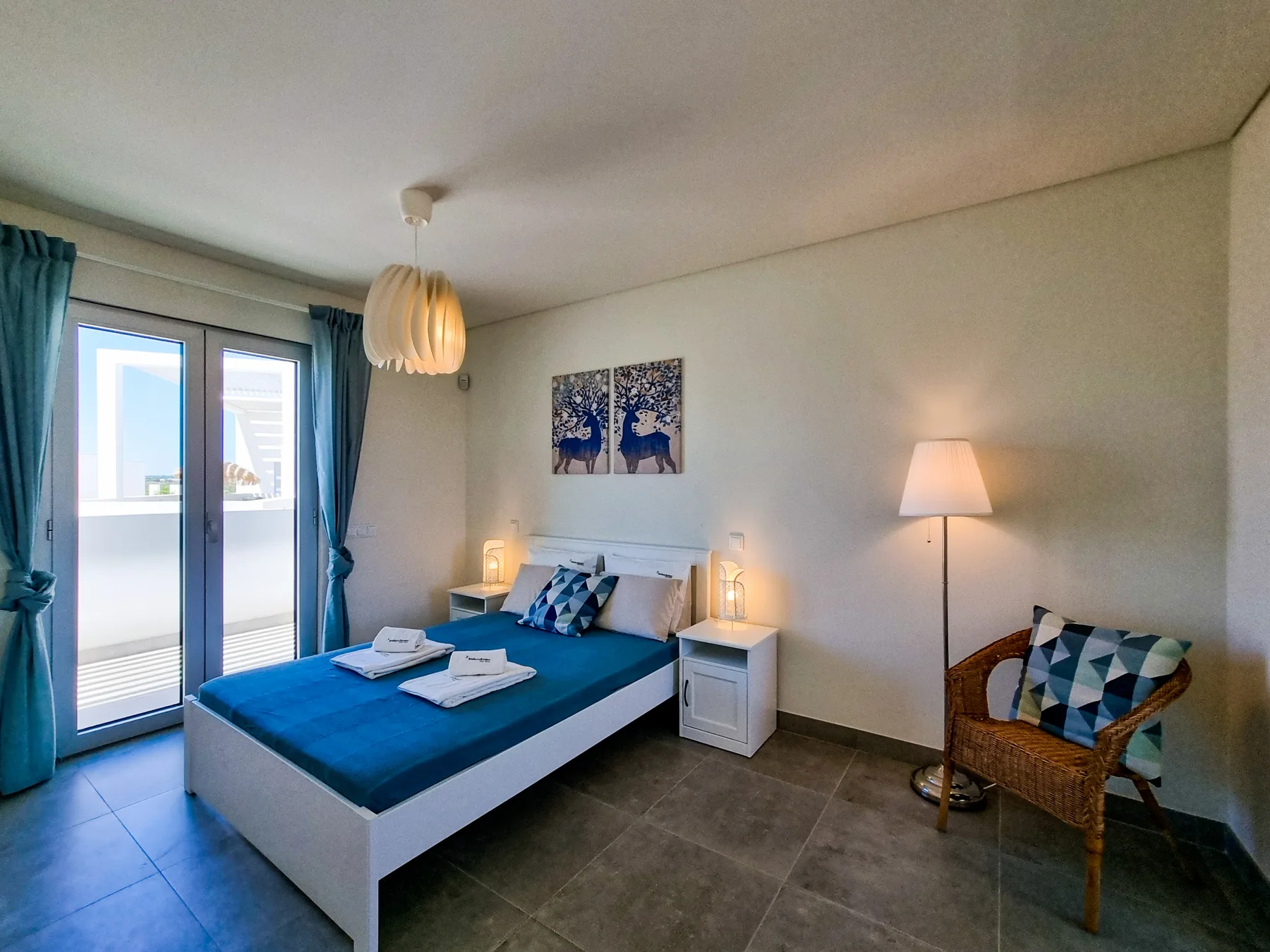A bedroom with a bed and blue curtains beside glass doors.