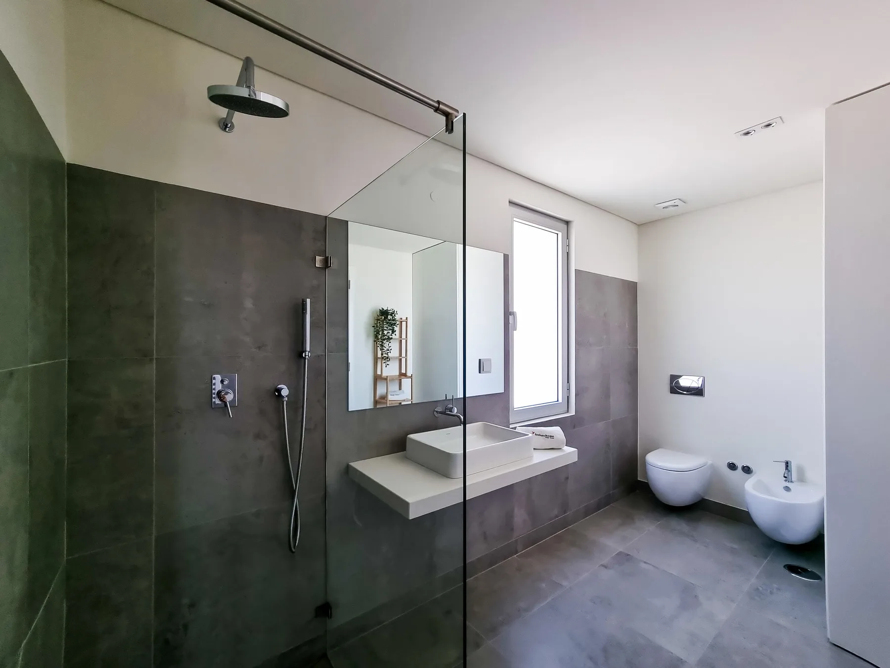 Un baño moderno cuenta con una ducha de vidrio, un lavabo sobre encimera y una ventana.