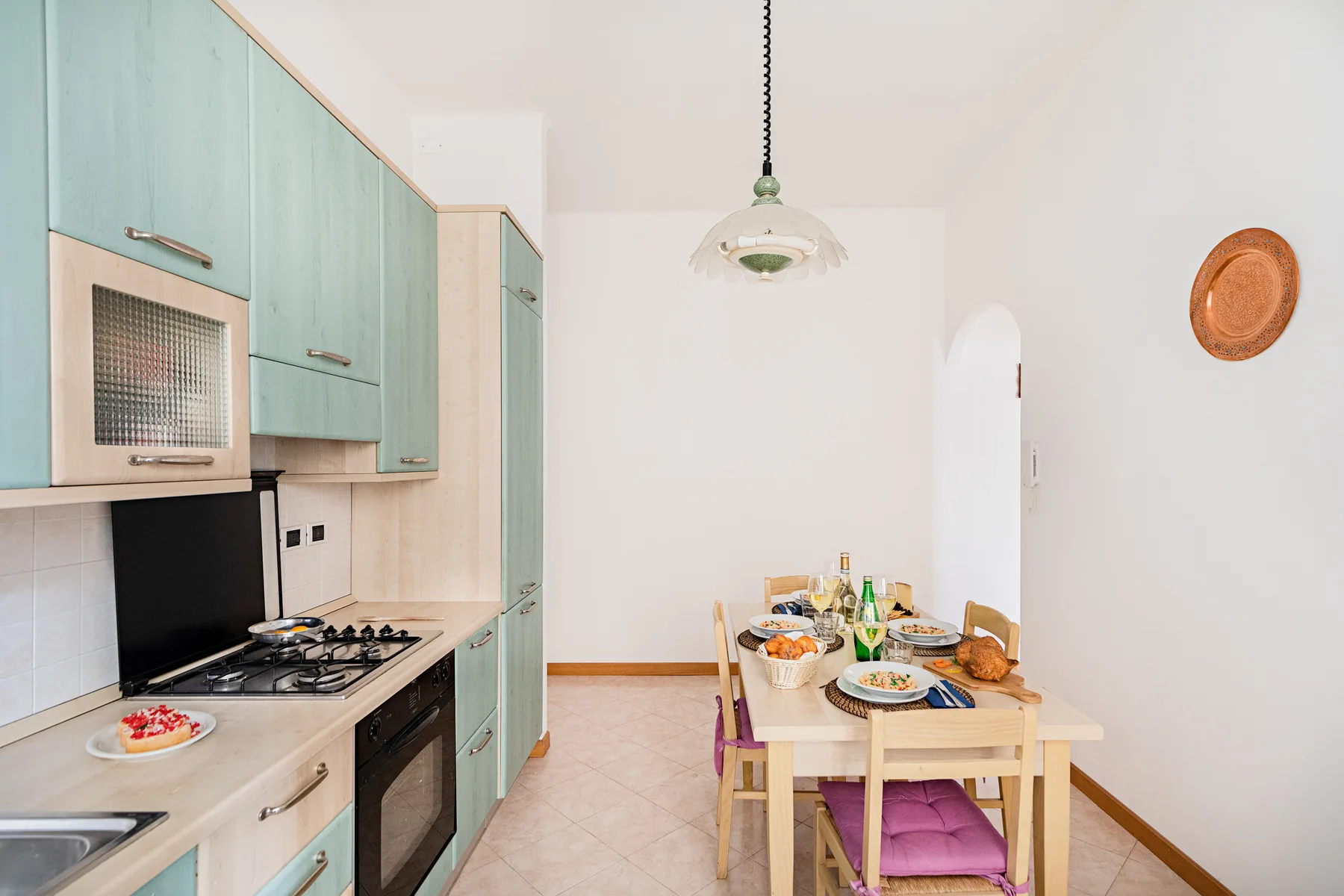 A bright kitchen and dining area with pale green cabinets and a set table.