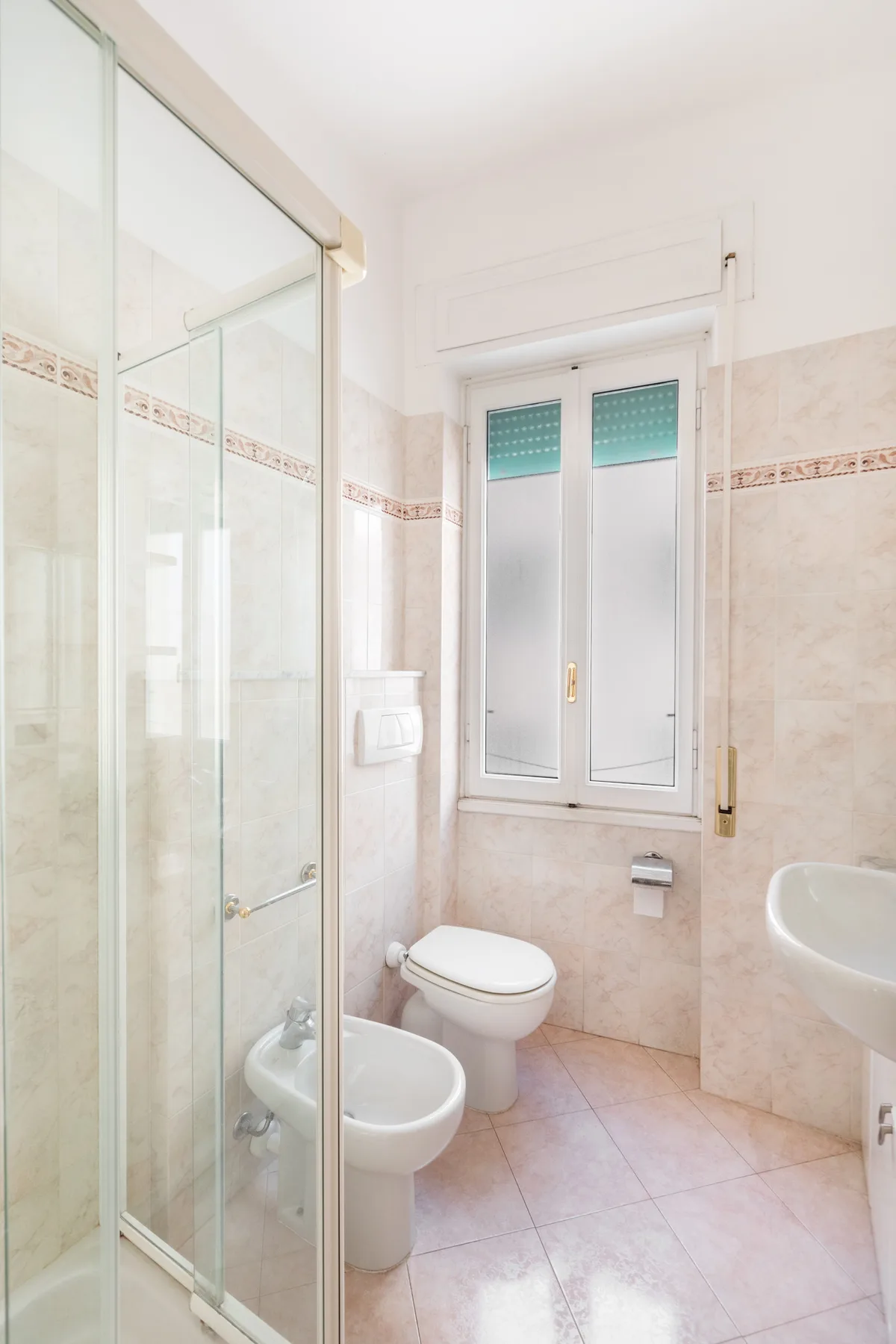 A bright bathroom with a glass shower, toilet, and window.