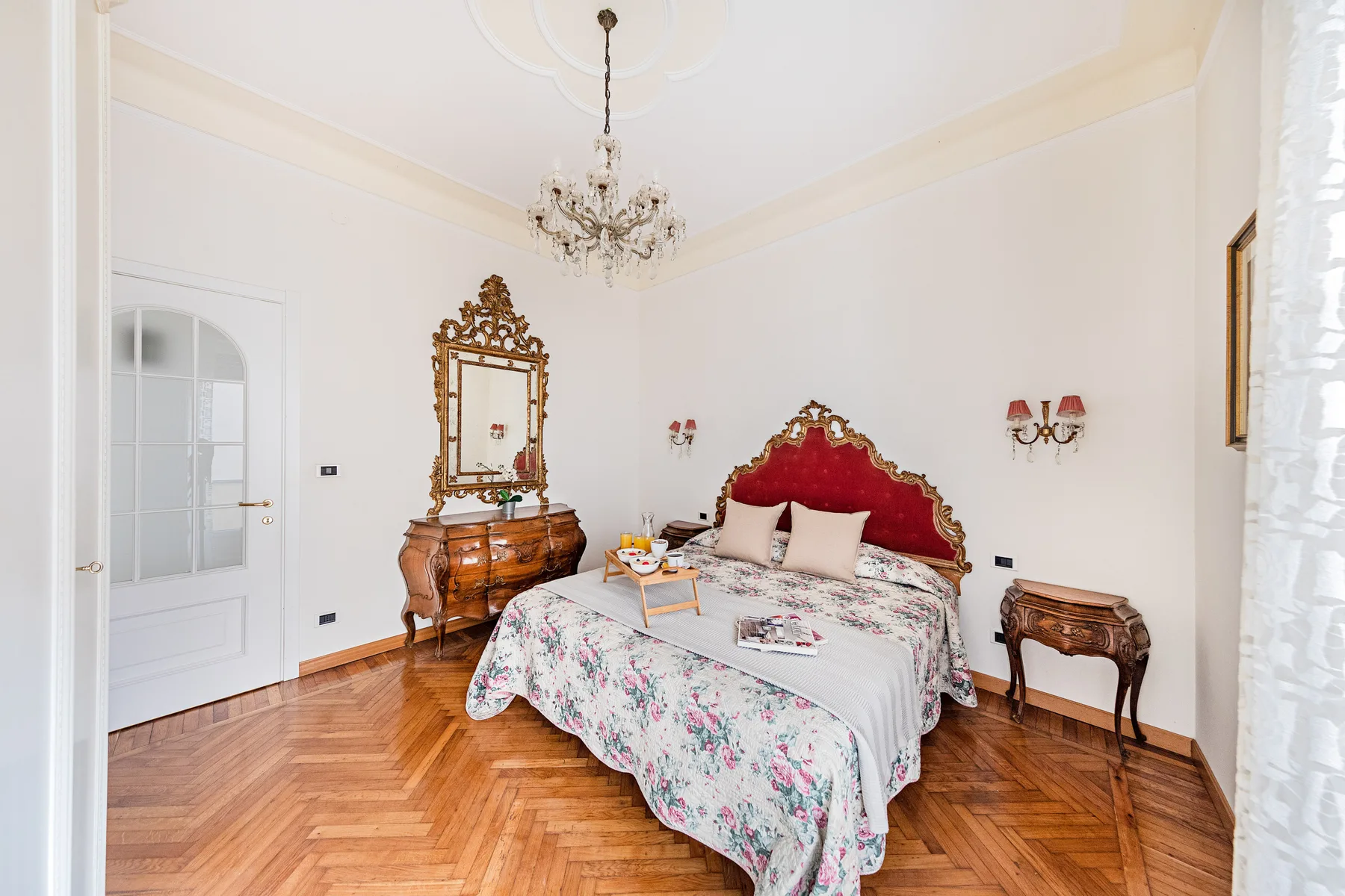 A bright bedroom with a floral bedspread and ornate wooden furnishings.