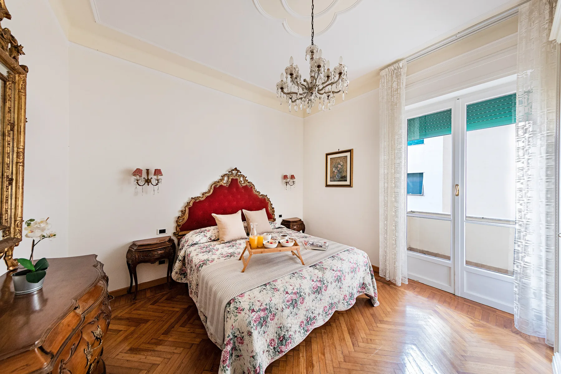A bedroom with a bed beneath a chandelier and glass doors opening onto a balcony.