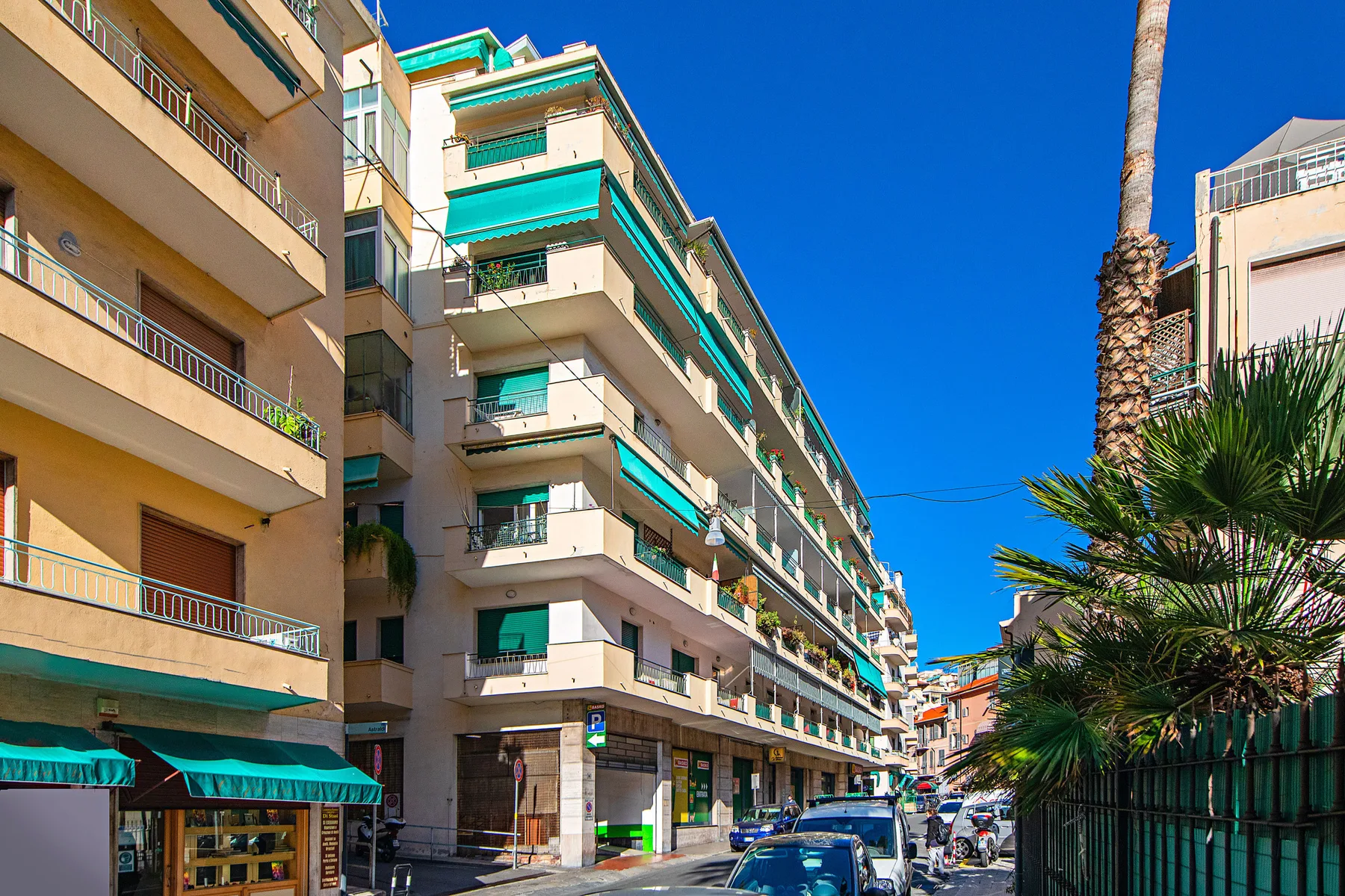 Apartment buildings line a sunny urban street beneath a clear blue sky.