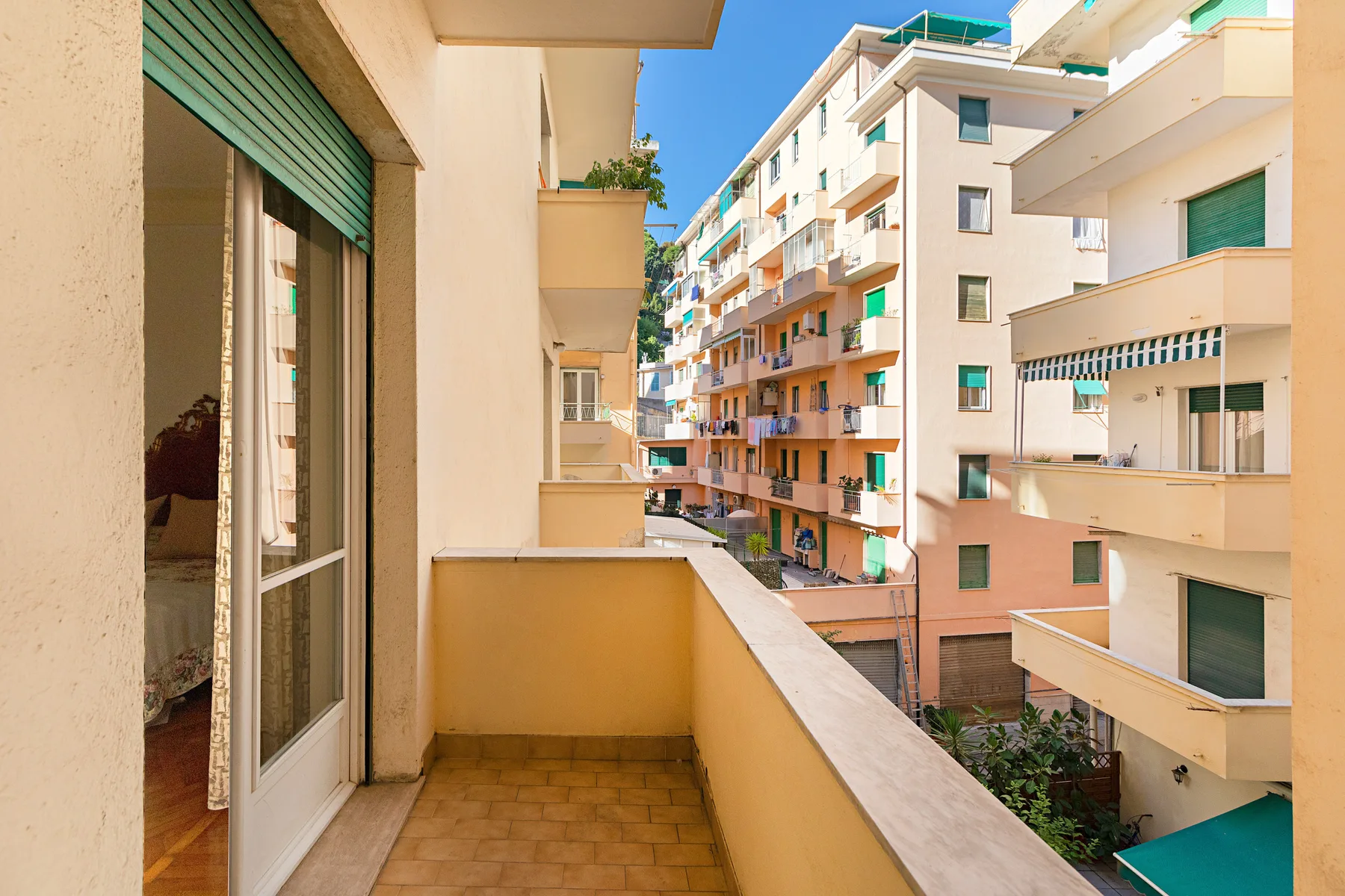 A balcony overlooks neighboring apartment buildings under a clear blue sky.