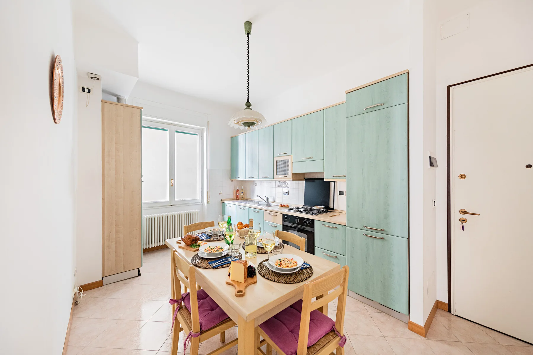 A bright kitchen and dining area with pale green cabinets and a set dining table.