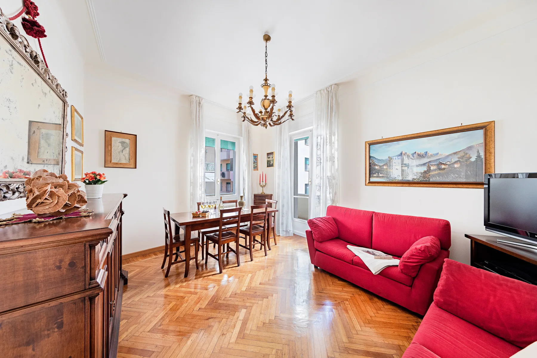 A bright living and dining room with red seating, a wooden table, and large windows.