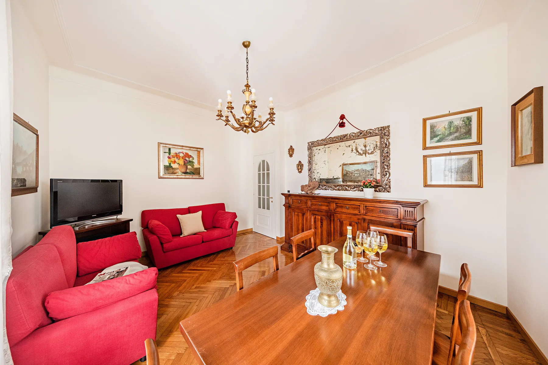 A living room with red seating, a wooden dining table, and a sideboard.