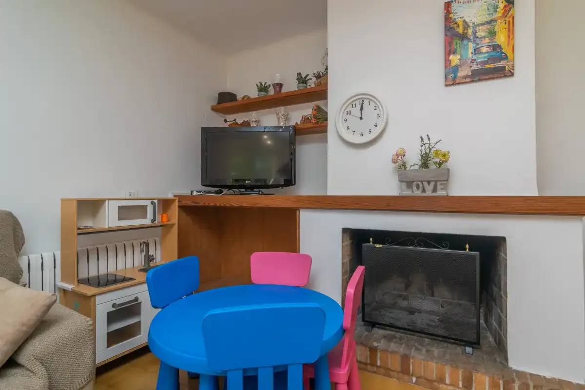 A living room with a television, a fireplace, and a small colorful table.