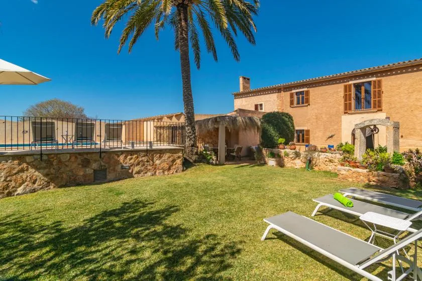 A sunny garden with a palm tree, lounge chairs, and a stone house.