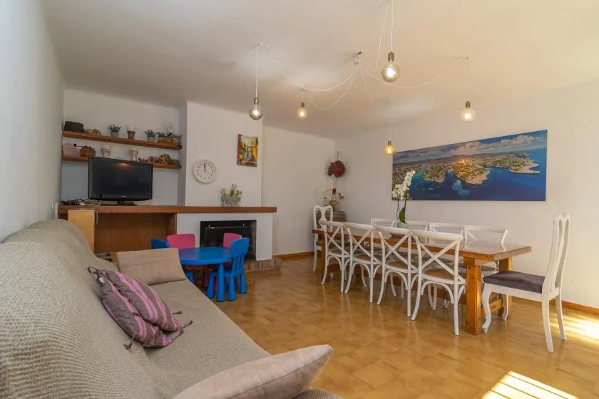 A living and dining area with a sofa, table, chairs, and wall-mounted television.