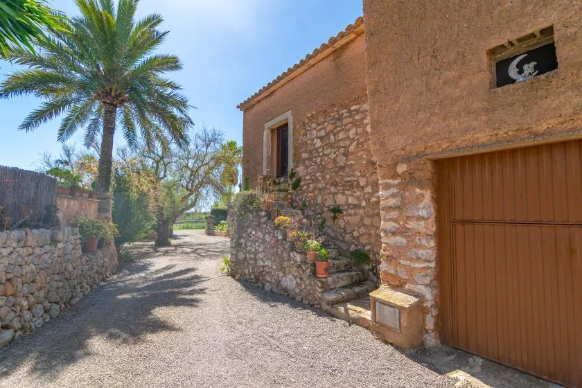 A gravel path runs beside a rustic stone building with a wooden garage door.
