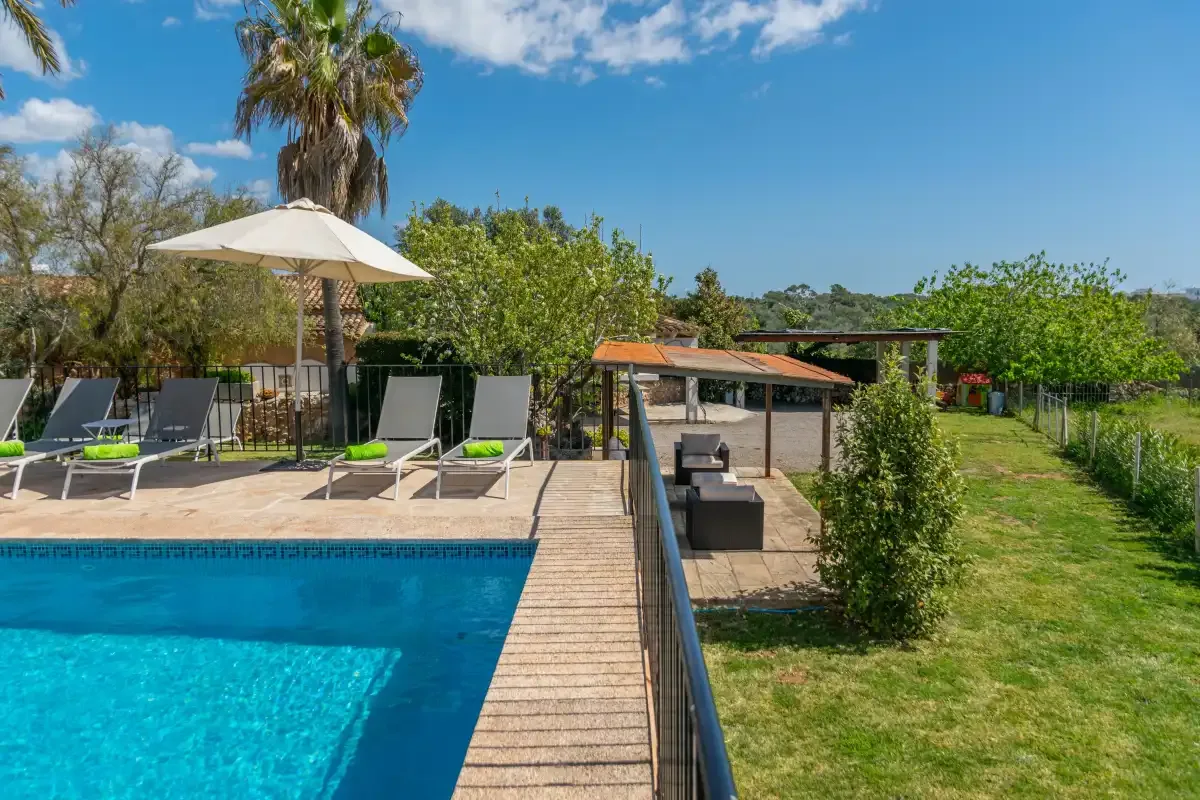 An outdoor pool beside a paved deck with lounge seating and a grassy garden.
