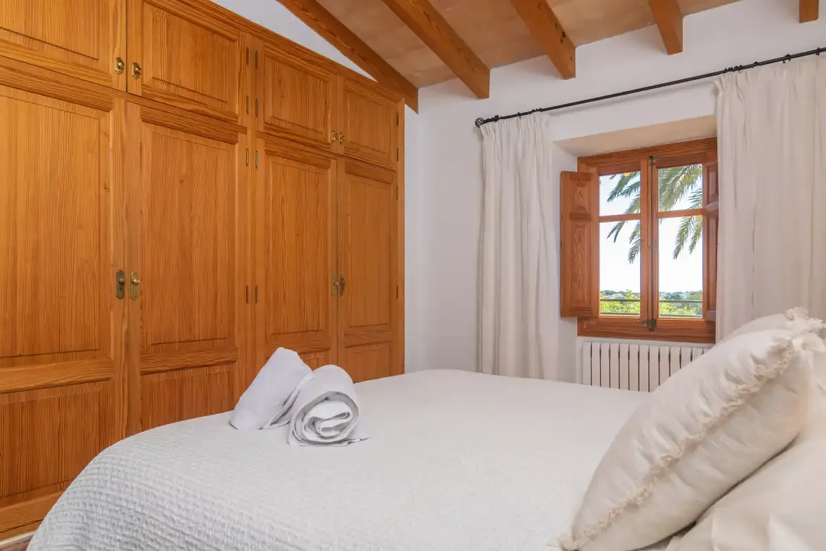 A bedroom with a bed, wooden wardrobes, and a window with curtains.