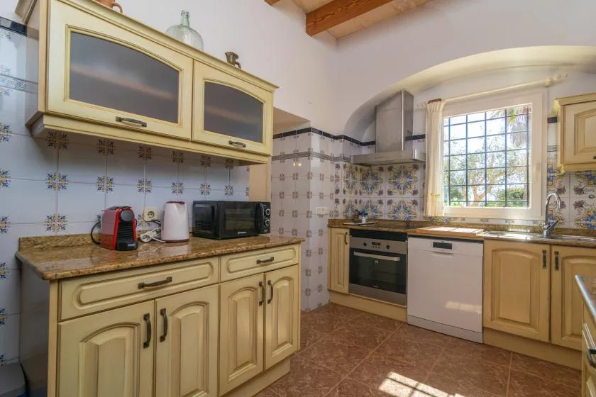 A kitchen with cream-colored cabinets, tiled walls, and a window above the sink.