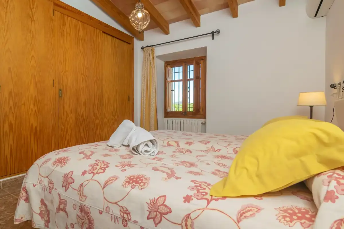 A bedroom with a floral bedspread and a wooden-framed window.