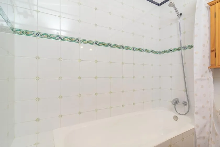 A tiled bathroom shower area with a handheld showerhead and bathtub.