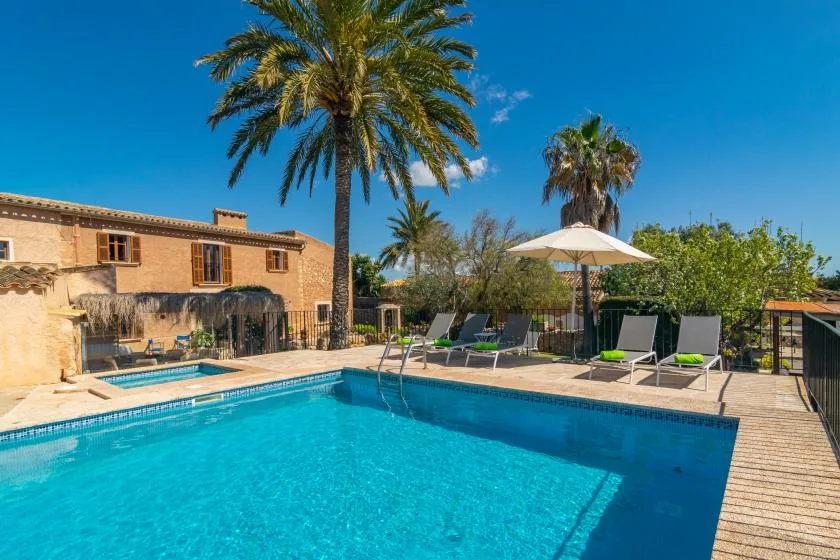 A swimming pool beside a stone building, with loungers and palm trees.