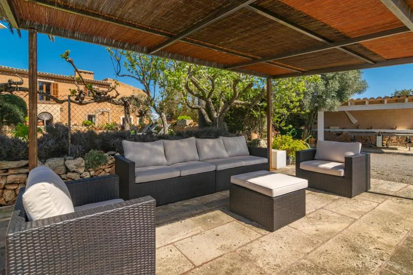A covered outdoor seating area with cushioned furniture and a stone-paved floor.