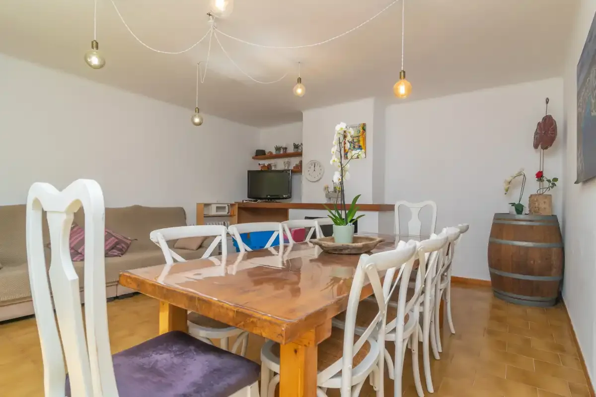A dining area with a wooden table and white seating beside a living area.